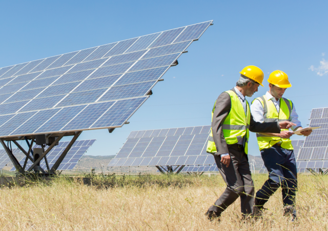 Workers reviewing an engineering report, with solar panels behind them