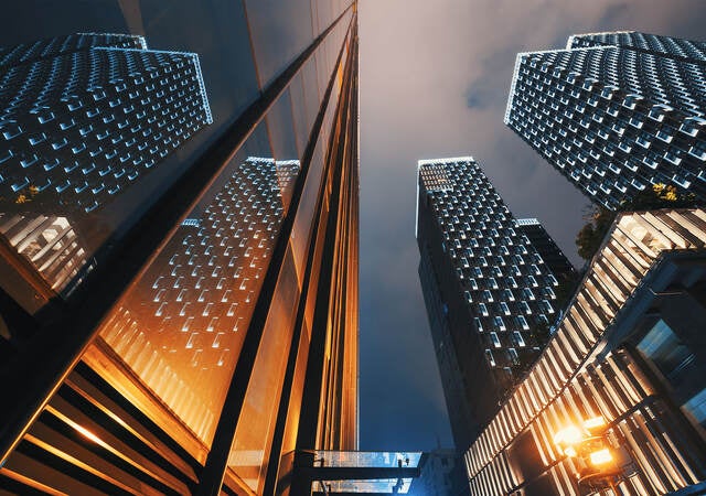 Low angle view of modern skyscraper buildings illuminated at night reflecting on a glass facade 