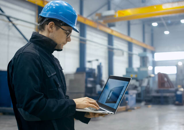 Factory worker in a hard hat is using a laptop computer with engineering software