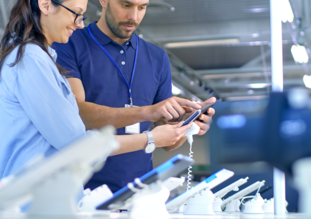 Electronics store employee shows a woman a new device.