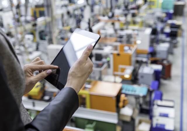 Manager reviewing a tablet while overlooking a factory floor