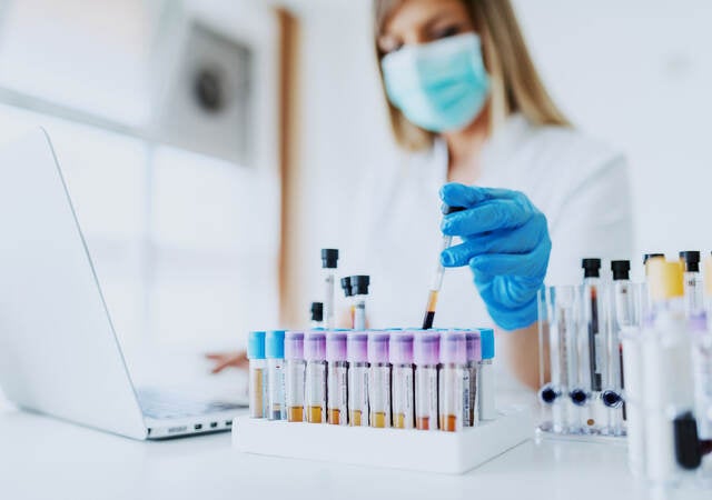 Laboratory technician working on laptop and handling test tubes