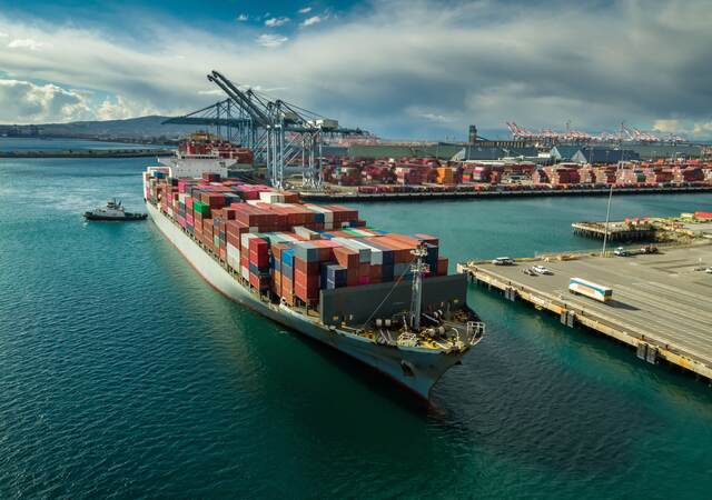 Tugboat maneuvering cargo ship at Dockside in Port of Long Beach.