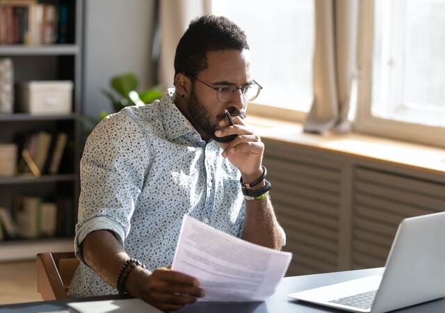 Person holding papers intensely looking at his open laptop