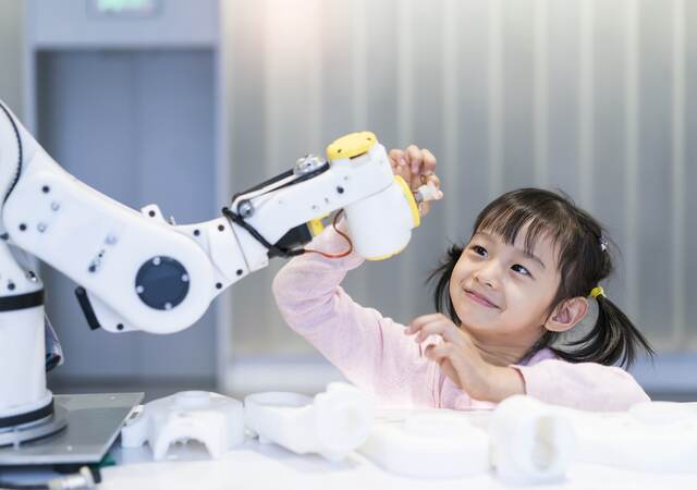 A young girl looking at a robotic arm.