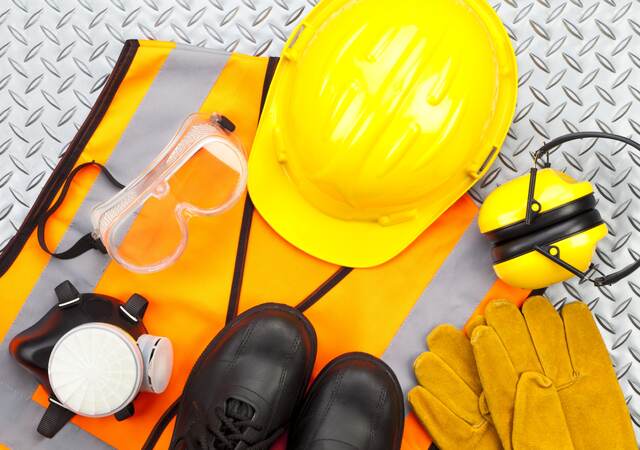 Industrial protective workwear shot from above on diamond-plate background. Includes hard hat, safety glasses, earmuff, gloves, respiratory mask, steel toe shoes and safety vest.