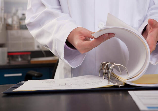 A close up of a lab worker’s hand flipping through three-ring lab binder