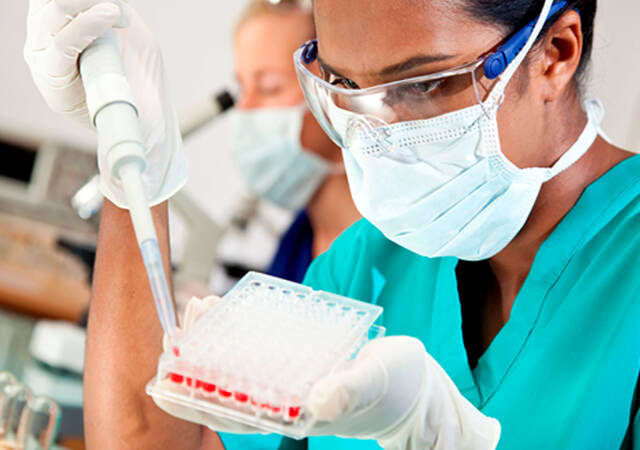 A lab worker in safety glasses and mask using large syringe to fill multicompartment test receptacle