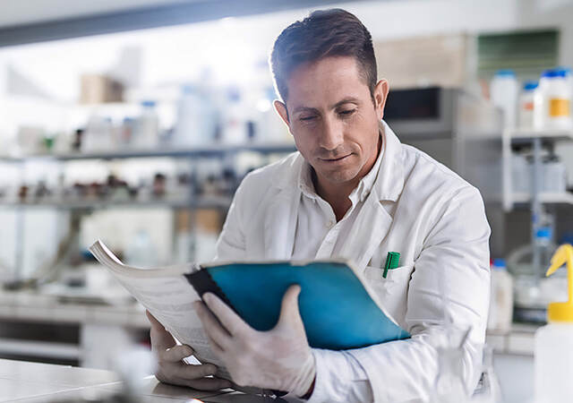 A laboratory worker sitting at a table reviews a guide