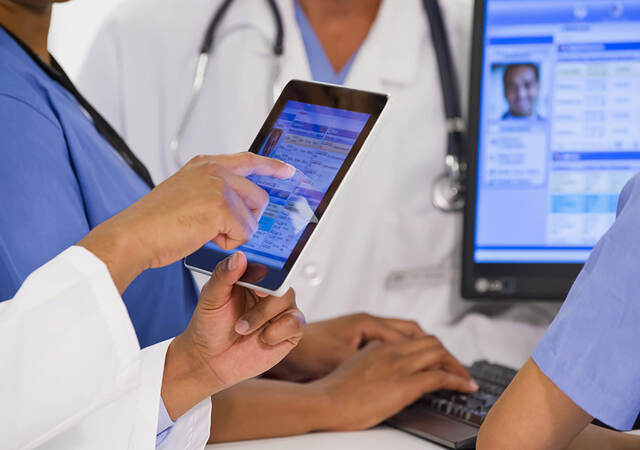 A close-up of a group of four co-workers sharing patient information on tablet and desktop screens