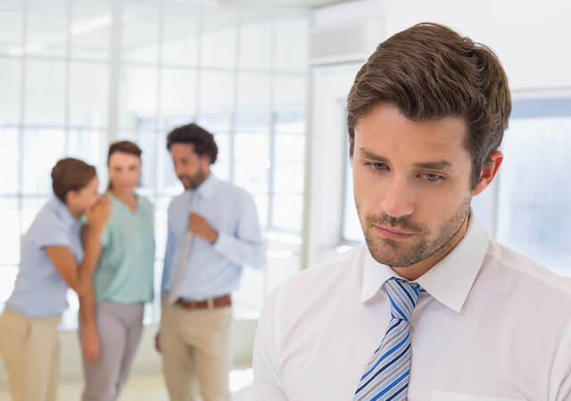 An employee in the foreground noticeably emotional while three coworkers whisper in the background