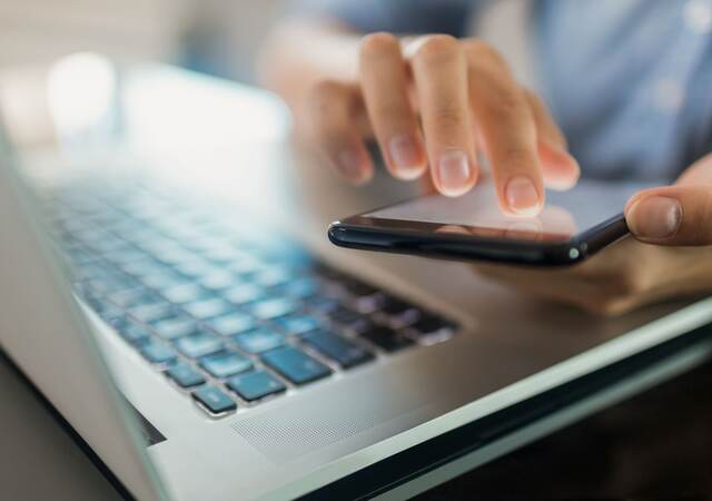 Close-up of a businesswoman using a phone and laptop.