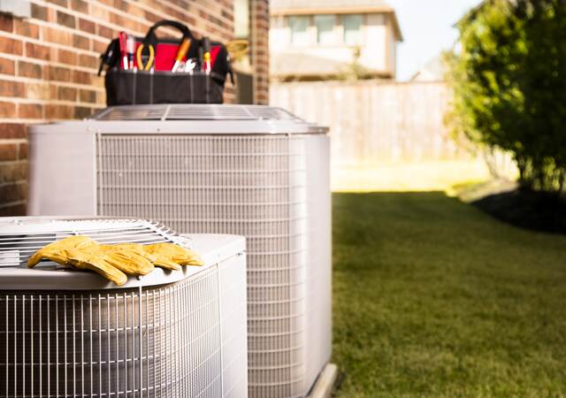 Bag of repairman’s work tools on top of air conditioner unit outside of residential home.