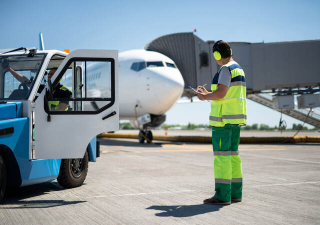 Worker taking notes at airfield while colleague sits in tug cab