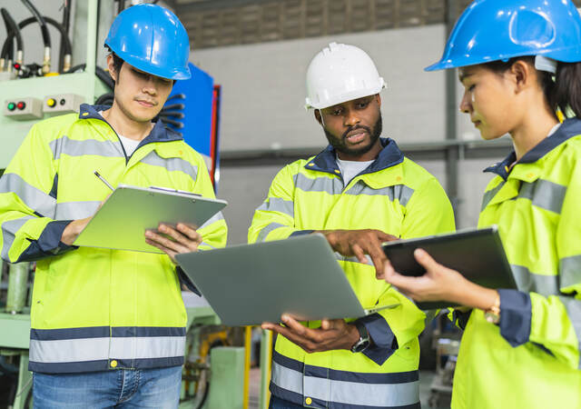 Workers in PPE holding clipboards and talking