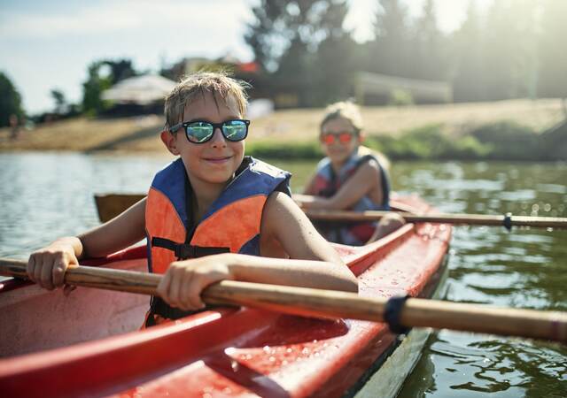 Children in life jackets rowing a canoe.