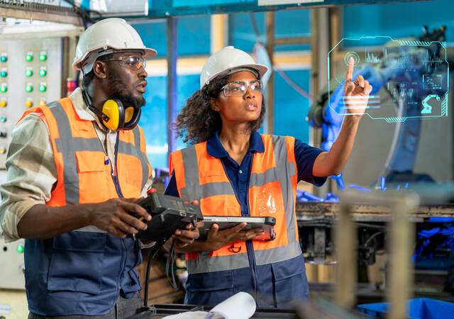 Engineer using tablet to check the robot system while her teamwork checks the security of the robot.