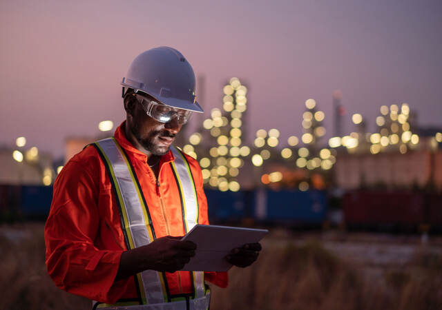 Engineer using tablet near an oil refinery at night