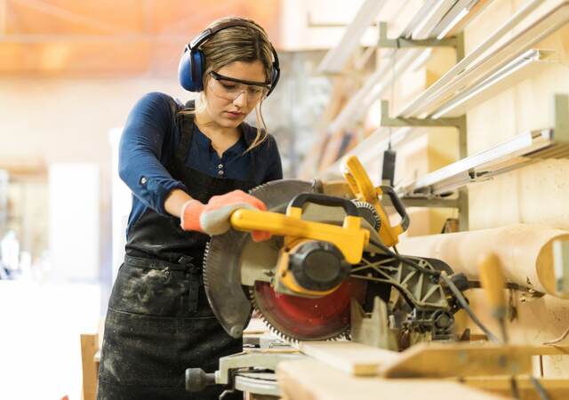 A female carpenter using a circular saw in a woodshop.