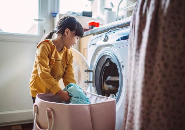 Little girl unloading the washing machine while helping her mom with laundry at home