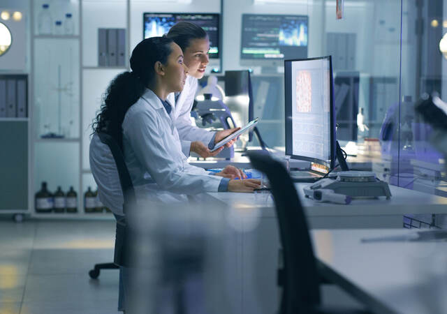 Two scientists in the lab viewing data on a laptop