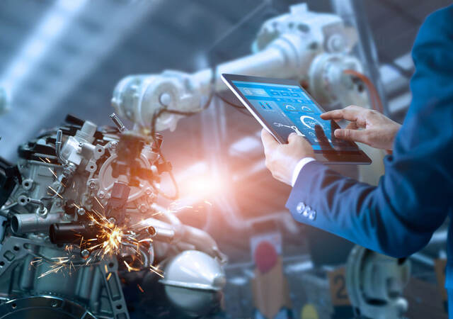 Person using tablet to control robotic arm in a factory