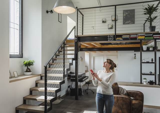 Young woman controlling smart home functions through mobile phone at modern home.