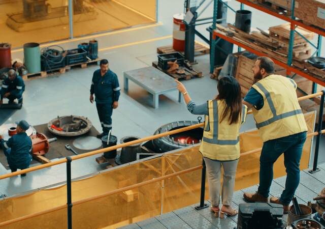 Managers at a manufacturing warehouse factory watching workers inside a capability building workshop.