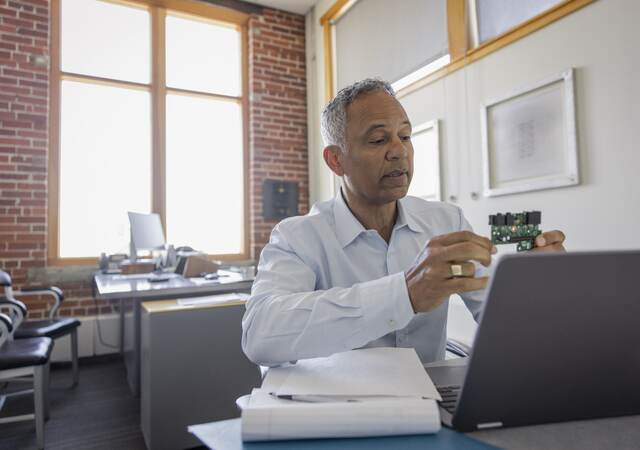 Male engineer at laptop explaining semiconductor on video call in meeting.