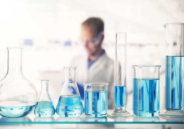 Close up of various solutions in beakers on shelf in lab.