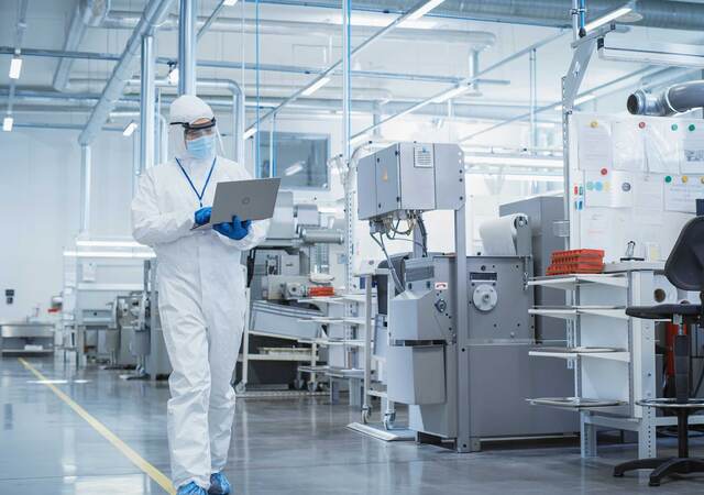 Person wearing PPE and walking through a lab while looking at a laptop