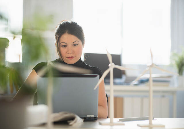 a person with small wind turbine models on a desk, working on a laptop