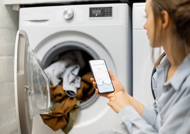 Woman controls washing machine with a smartphone.