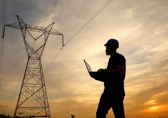 Electrical engineer while working laptop while looking at a power station at dusk