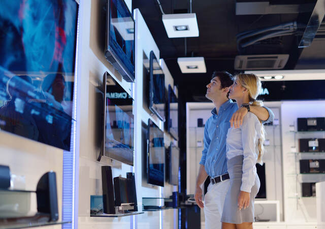 A couple in an electronics store looking a televisions