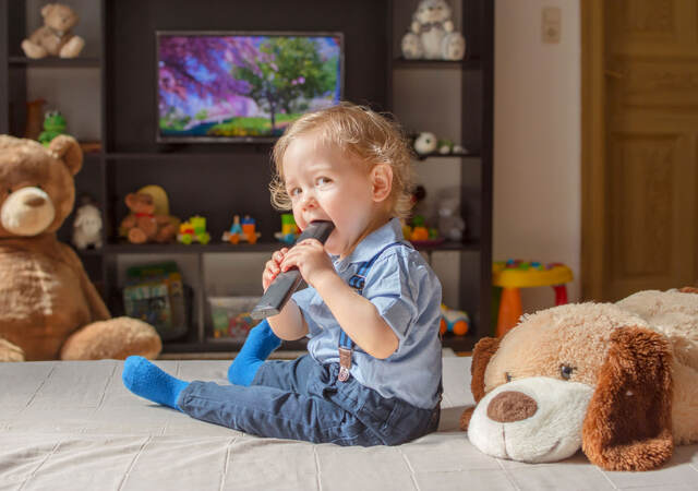 Toddler sitting while chewing on a tv remote