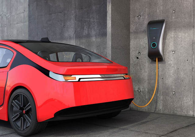 A red electric vehicle is charging at a wall charger