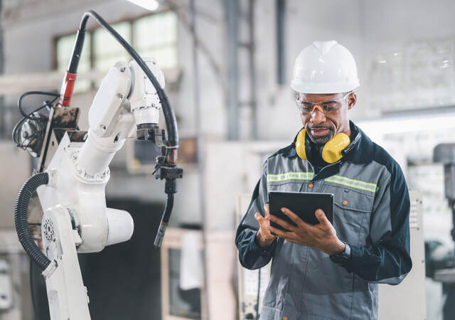 Engineer working on a tablet in front of a mechanical arm in a factory