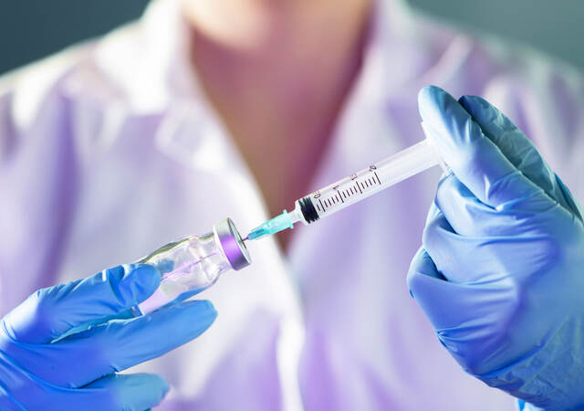 Closeup of a medical professional's hands in blue gloves holding syringe and vial.