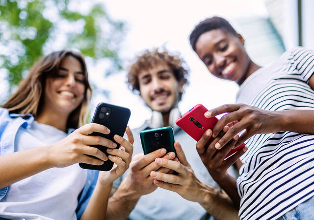 Three smiling friends outdoors and holding cellphones