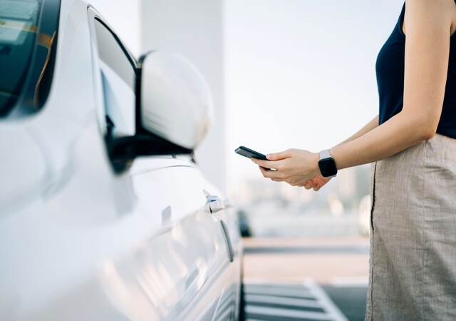 Close up of young Asian woman using mobile app device on smartphone to unlock the doors of her car in a car park.