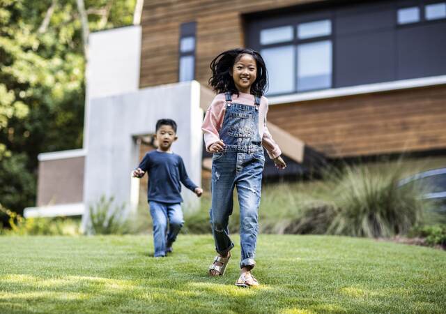 Brother and sister running in front yard of modern home.