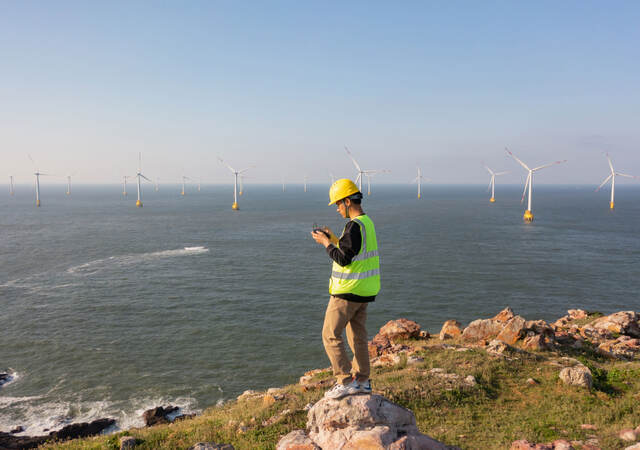 Engineer reviewing data on the coast while overlooking a wind farm at sea