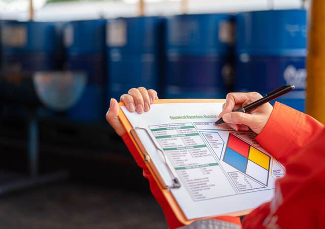 Worker checking chemical hazardous communication form on a clipboard.