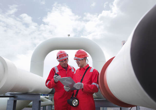 Two engineers having a discussion in front of pipes at a gas storage plant