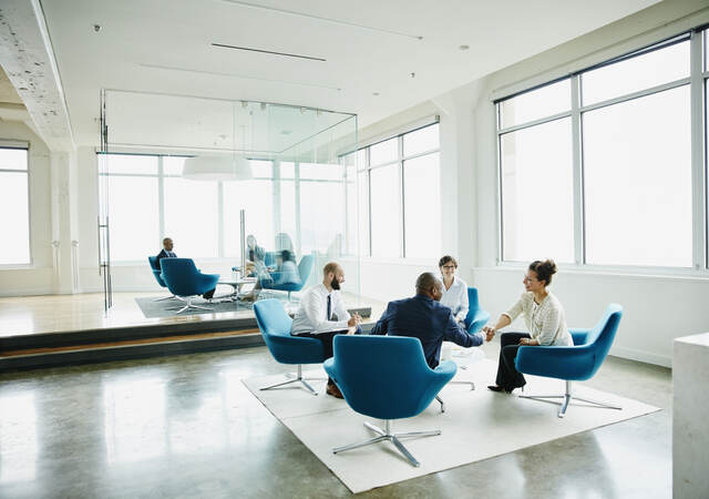 Business professionals sitting in blue chairs having a meeting in a white, modern office