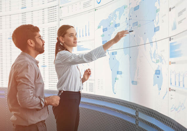 Two workers standing in front of a large monitor