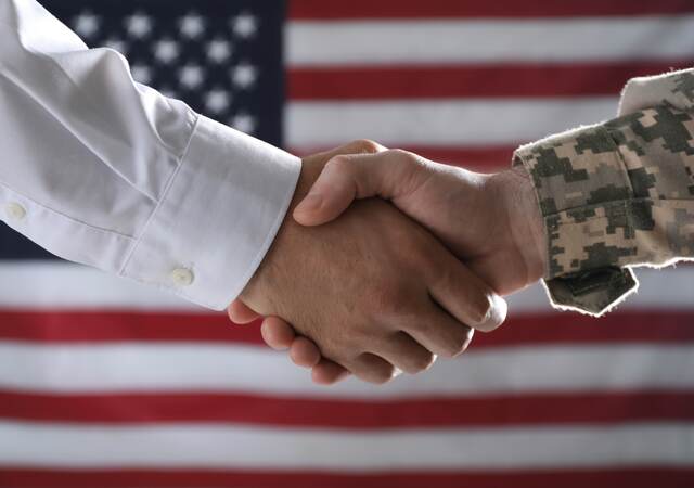 Military personnel shaking hands in front of an American flag