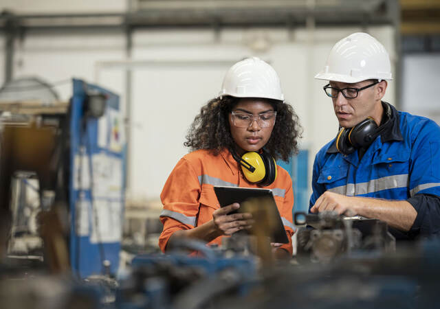 Two manufacturing process engineers in a factory looking at a tablet together.  