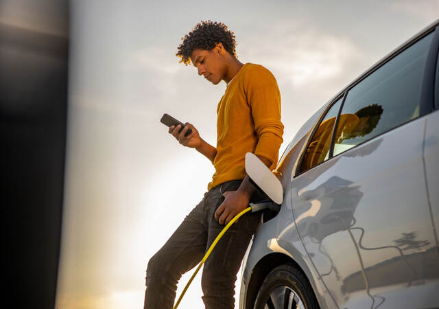 A young person leaning against a car and looking at a mobile device